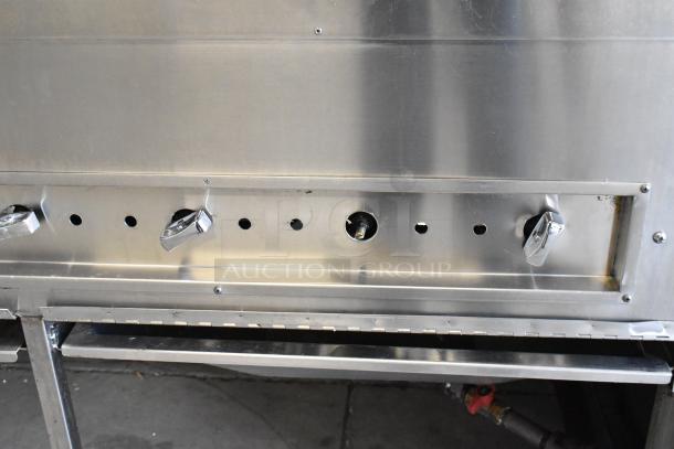 Stainless steel commercial gas-powered grill with control knobs, on commercial casters, in good condition.