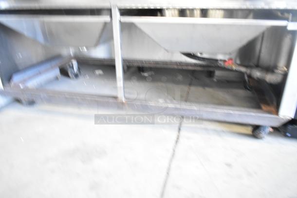 Stainless steel commercial gas grill on casters, undercarriage visible, showing durable construction and mobility.