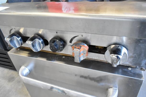 Stainless steel commercial gas-powered 4 burner range with oven, featuring sturdy dials, in used but functional condition.