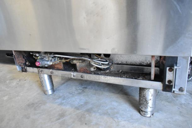 Stainless steel commercial gas-powered 4 burner range with oven, showing lower section and gas connections, in used condition.