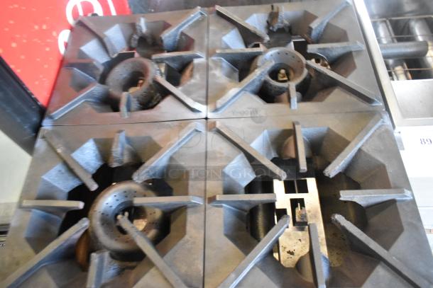 Stainless steel commercial gas-powered 4 burner range with oven, showing sturdy cast iron grates, in used condition.