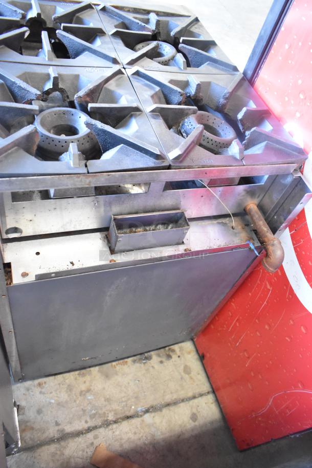 Stainless steel 4-burner gas range with oven, commercial use, visible wear, sturdy grates, built-in gas connection.