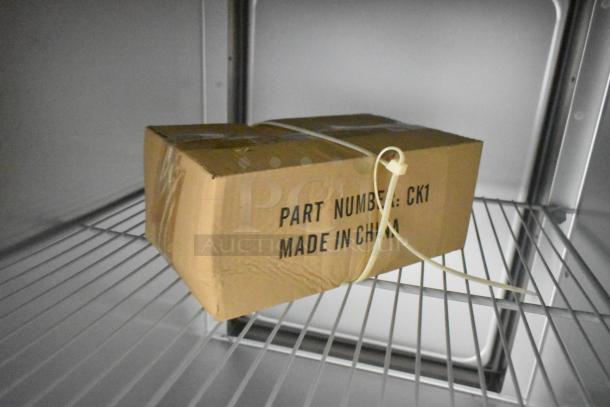 Inside of a Traulsen G10042-032 cooler, featuring poly-coated racks with a cardboard box labeled "Part Number: CK1 Made in China."