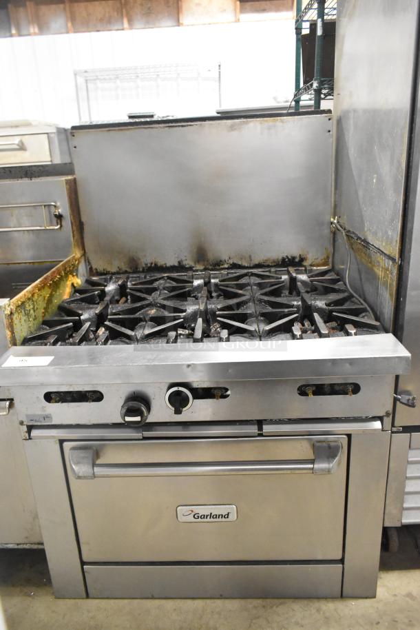 Garland stainless steel commercial gas range with 6 burners, oven, and backsplash. Used condition. Brand logo visible.