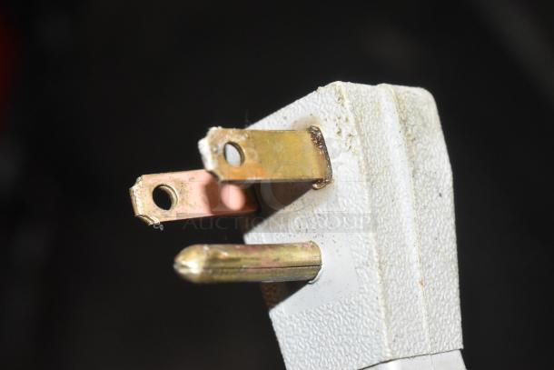 Close-up of a three-prong power plug, showing wear and slight discoloration on the metal prongs.