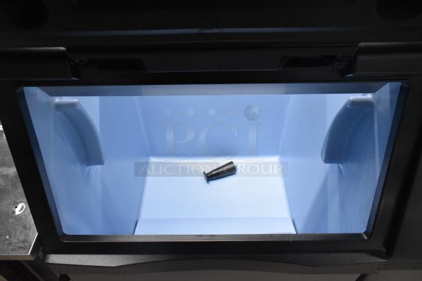 Stainless steel commercial ice bin with blue interior, open lid view, appears in good condition. Includes small black component inside.