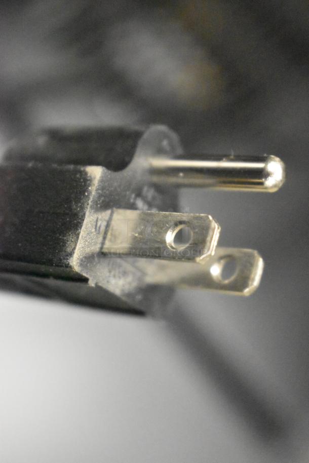 A close-up of the plug for the Galaxy 177CRG2B black refrigerated merchandiser, showing the prongs and part of the cord.