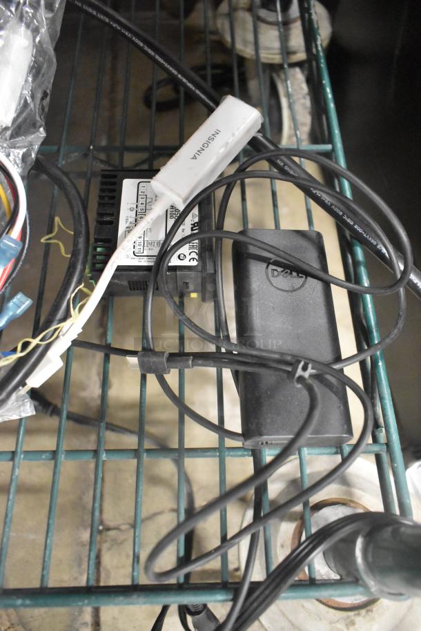 Assorted wires and devices, including Insignia adapter and Dell power supply, in used condition, on a metal rack.