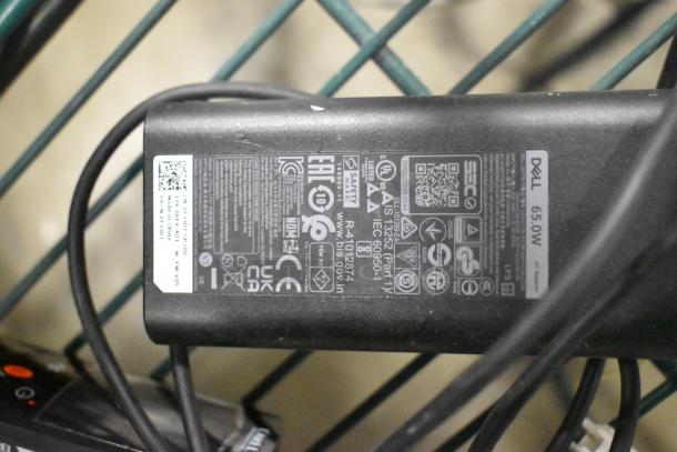 Dell 65W AC adapter with visible label displaying model details and safety certifications, surrounded by wires.