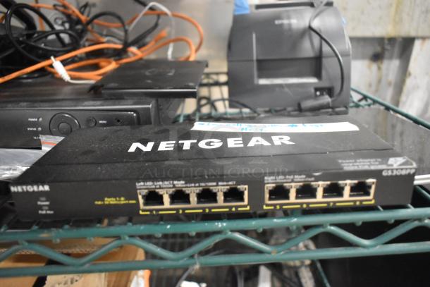 Netgear GS308PP 8-Port Gigabit Ethernet switch on shelf, with cables and receipt printer in background.