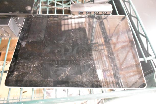 A dusty black electronic device on a wire shelf, connected to a multi-port USB hub.