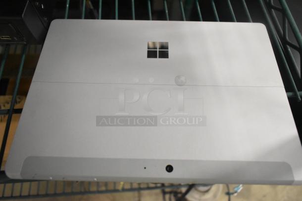 Silver laptop with a Windows logo, resting on a metal shelf. Marks and ports visible on the bottom edge.