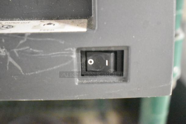 Close-up of a power switch on a scratched, gray electronic device. Marks indicate wear. Tags suggest paper feeder function.