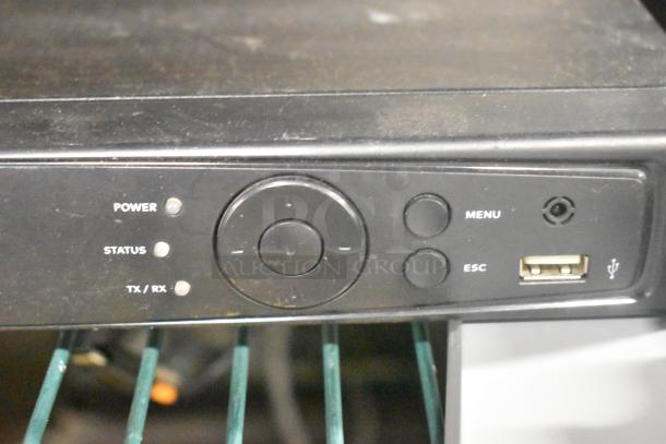 Front panel of a black electronic device showing power, status, TX/RX indicators, menu and escape buttons, and a USB port.