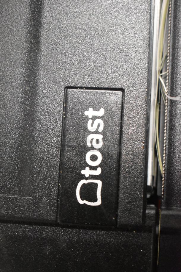 Black Toast-branded device panel, possible receipt printer, textured surface, visible wiring to the side.