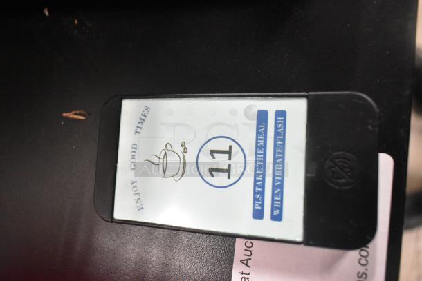 Pager system with charger, showing one pager labeled "11." Text reads "Pls take the meal when vibrate/flash." Black casing.