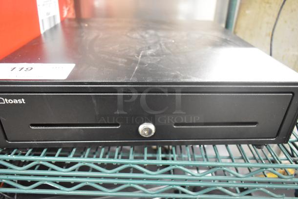Toast metal cash drawer in black, featuring key lock and two slots. Slight surface wear visible on top.