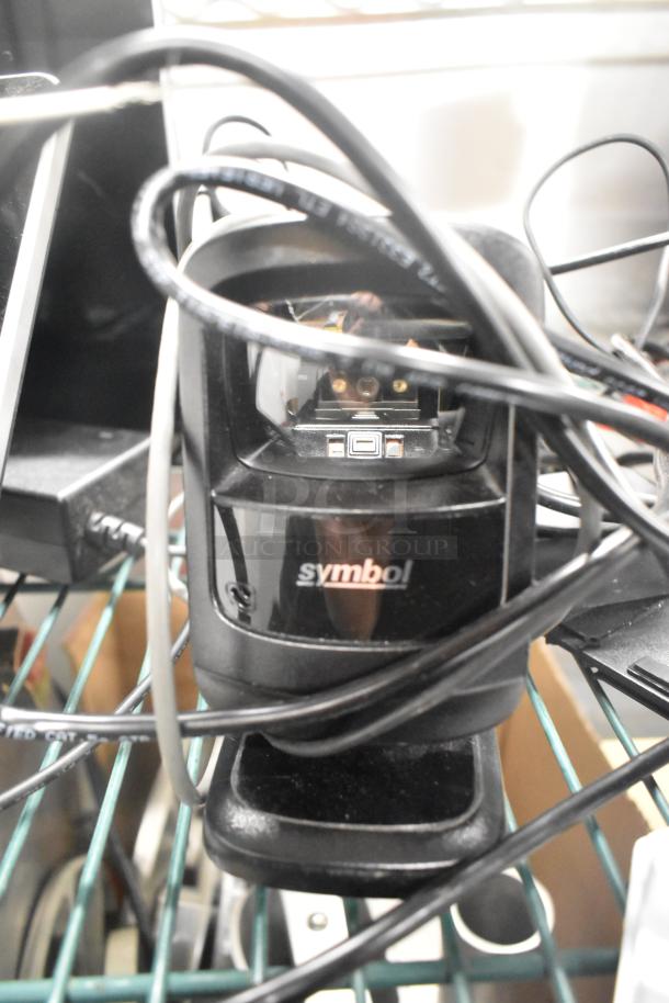 Close-up of a Symbol barcode scanner with visible cables, part of a set including Toast POS monitors and a card reader.