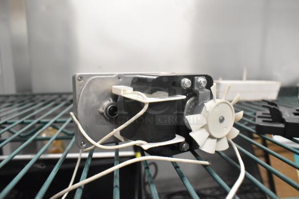 Motor with fan and attached wires, in good condition, placed on a metal rack.