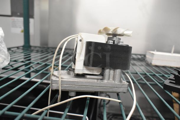 Metallic motor with attached wires and plastic propeller, resting on a shelf. Appears in used condition.