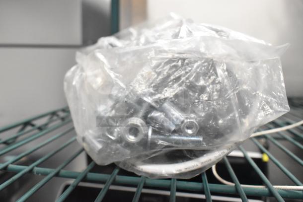 Bag of metal bolts and nuts, sealed in plastic, on wire shelf, part of "3 Various Items Including Motor" auction lot.