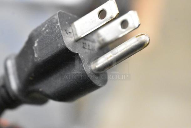 Close-up of the plug for a Keurig K150 coffee machine, featuring a standard three-prong design.