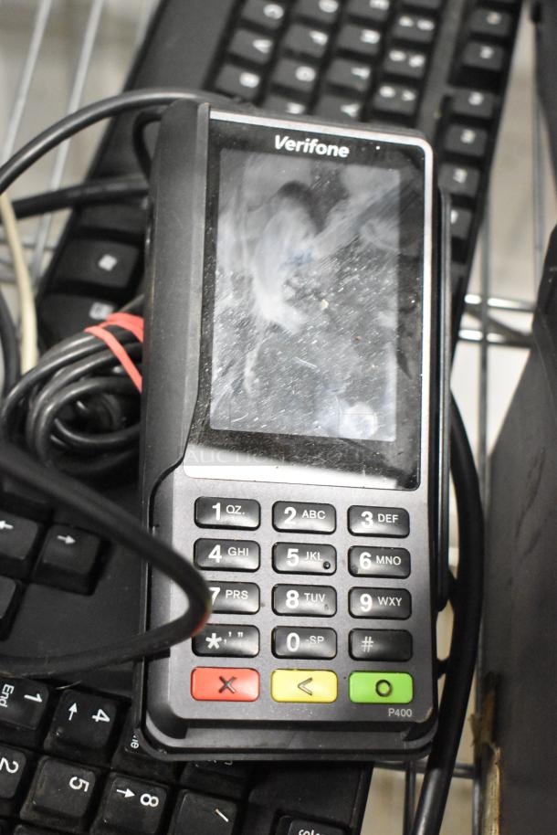 Verifone P400 payment terminal with visible wear, tangled cables, on a stack of keyboards.
