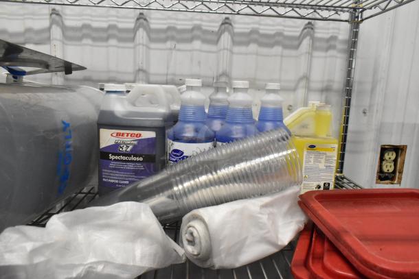 Tiered lot with poly bins, red lids, Betco Spectaculoso lavender cleaner, plastic cups, and various cleaning products.