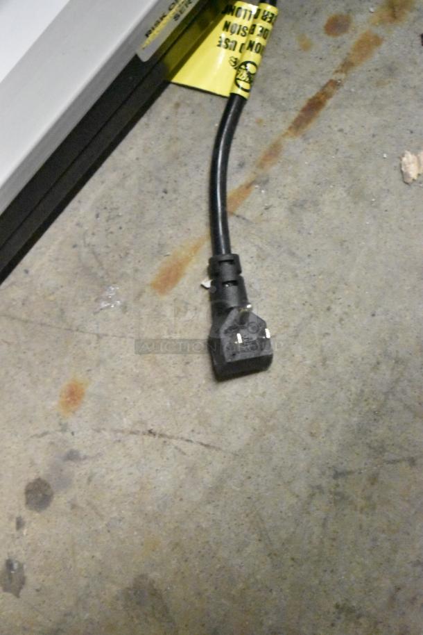 Power cord on concrete floor, near a device with a partially visible yellow caution label.