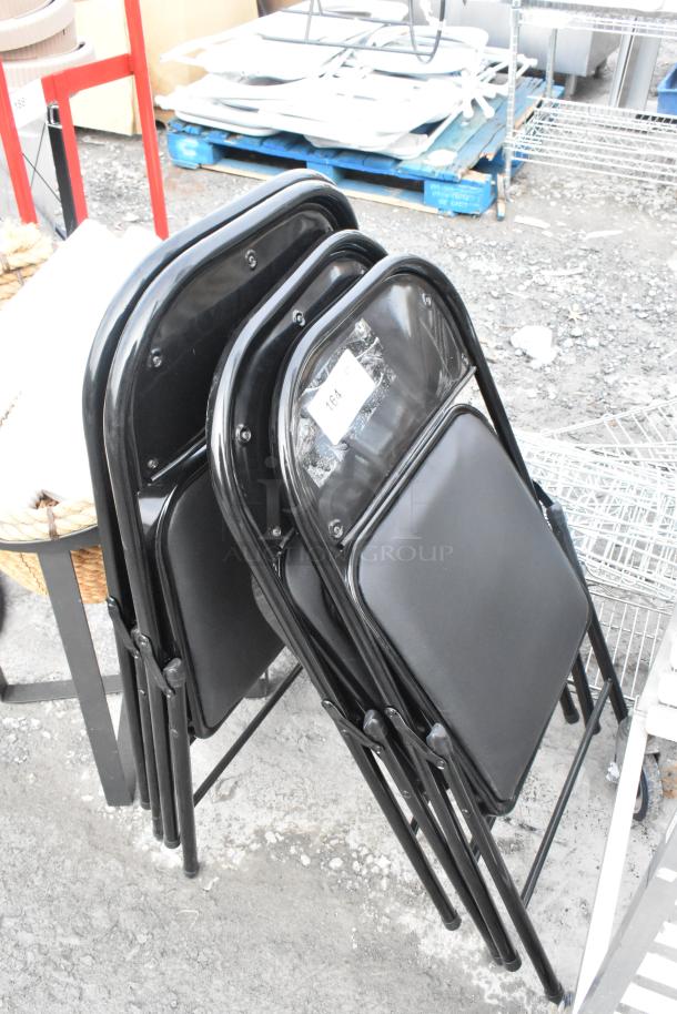 4 black metal folding chairs, stackable, with padded seats in good condition. Auction tag labeled "164" attached.