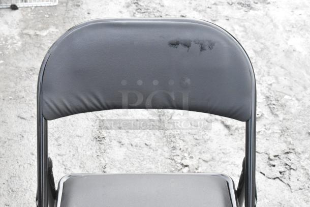Black metal folding chair with some wear on the seat back. Durable design, ideal for indoor and outdoor use.