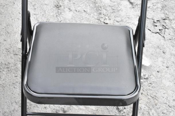 4 black metal folding chairs with cushioned seats, minimal wear, sturdy build, ideal for events or outdoor use.