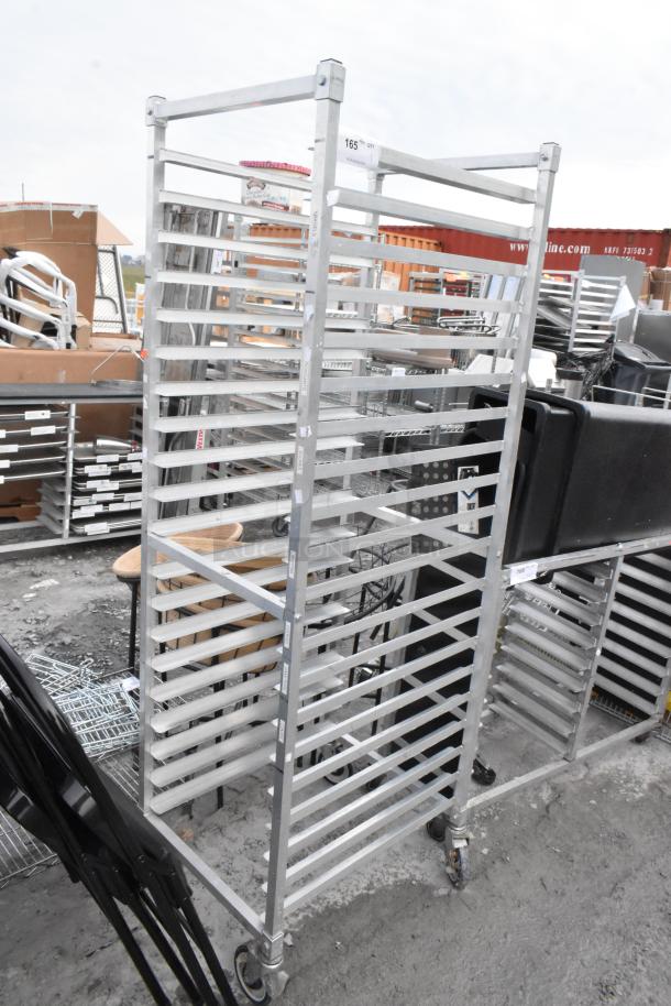 Metal commercial pan transport rack with multiple slots, on heavy-duty casters, in used condition; ID tag visible.