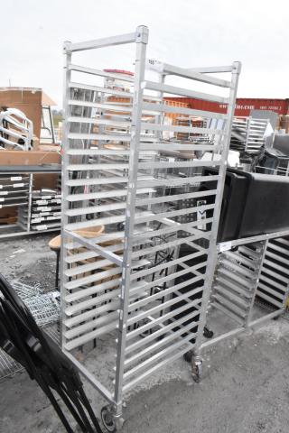 Metal commercial pan transport rack with multiple slots, on heavy-duty casters, in used condition; ID tag visible.