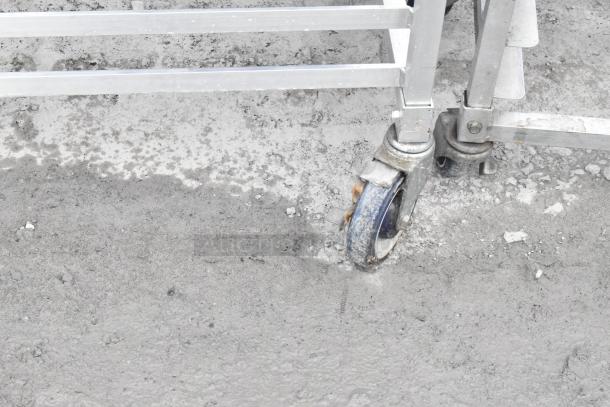 Metal commercial pan transport rack on sturdy commercial casters, showing signs of wear. Ideal for industrial kitchen use.