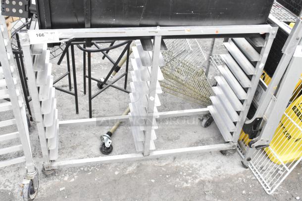 Metal commercial double pan transport rack on casters with two black trash cans and various contents. Visible wear on frame.