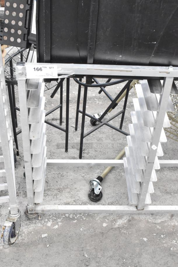 Metal commercial double pan transport rack on casters, includes two black trash cans, visible shelving slots, used condition.