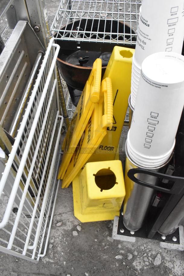 Assorted items including yellow wet floor caution cones, cup dispenser, and metal wire shelving. Items are in used condition.