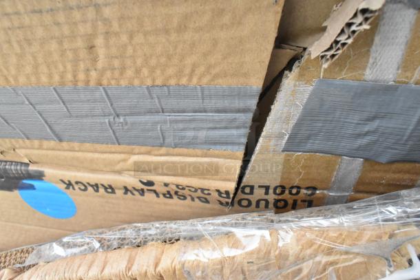 Cardboard packaging with duct tape shows "Liquor Display Rack," indicating 12 new scratch and dent items, including a Regency 600LDR stainless steel rack and white poly trash cans.