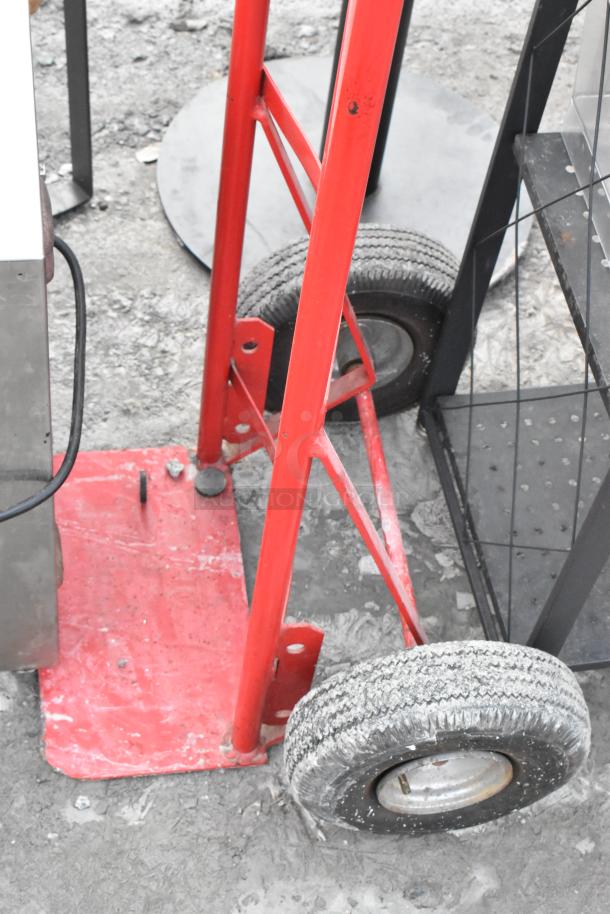 Red metal furniture dolly with two large rubber wheels, showing wear on wheels, sturdy construction for heavy lifting.