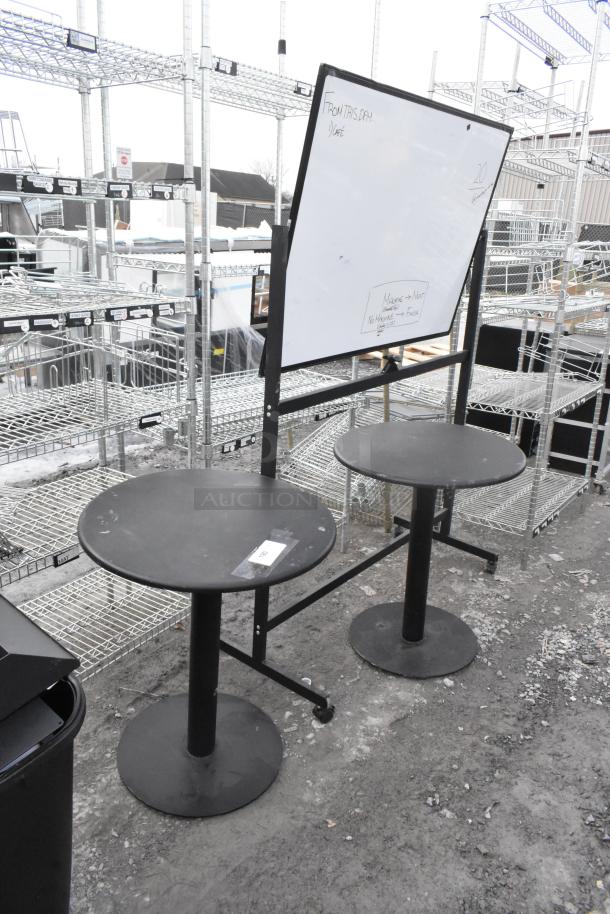 Three-item auction: two round black tables, one with tag, and a white board on stand with caster wheels. Basic condition.