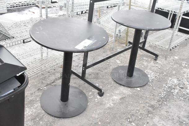 Two round black tables with pedestal bases, slight surface wear. Includes tag indicating multi-item auction.