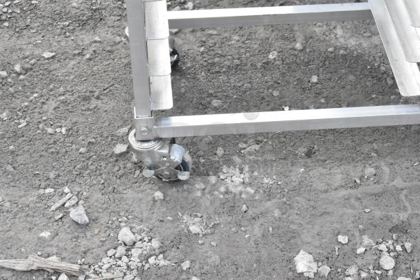Metal commercial double pan transport rack with casters, shown on gravel surface.