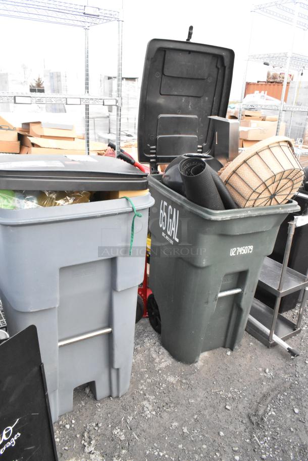 Two poly trash cans containing baskets and floor mats. One can labeled "65 GAL." Items in used condition.
