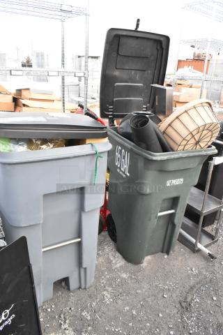Two poly trash cans containing baskets and floor mats. One can labeled "65 GAL." Items in used condition.