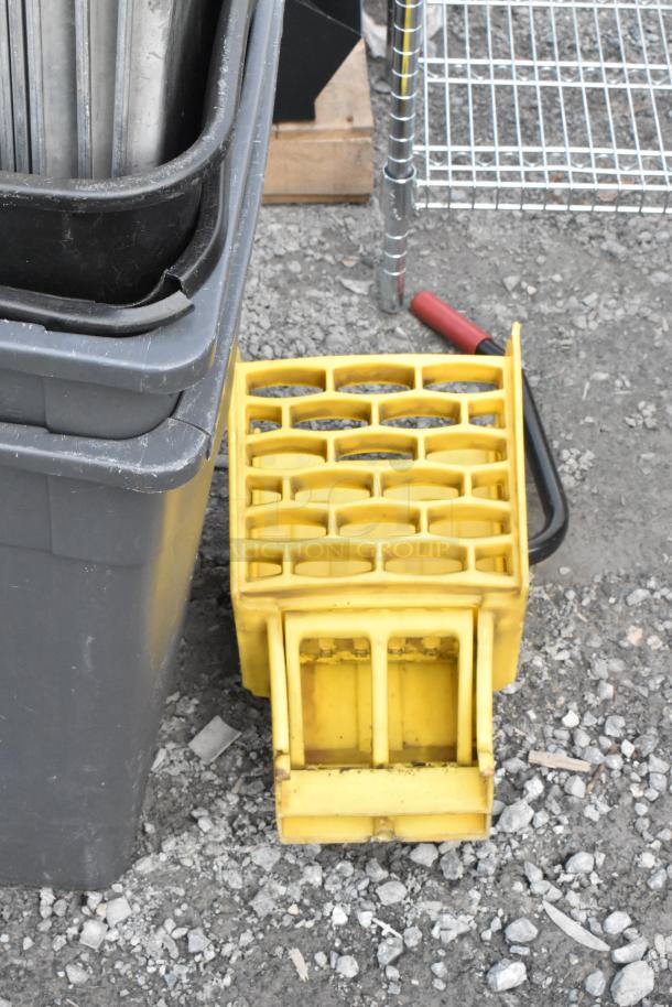 Lot of items including Poly Slim Jim trash cans, yellow crate, metal pans, and metal shelving on gravel surface.