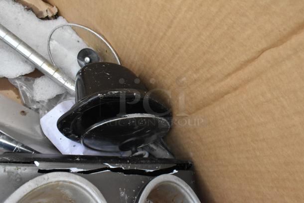 Cardboard box with black kitchenware, a metal pole, and baking pans. Items show scratches and dents, indicating minor damage.