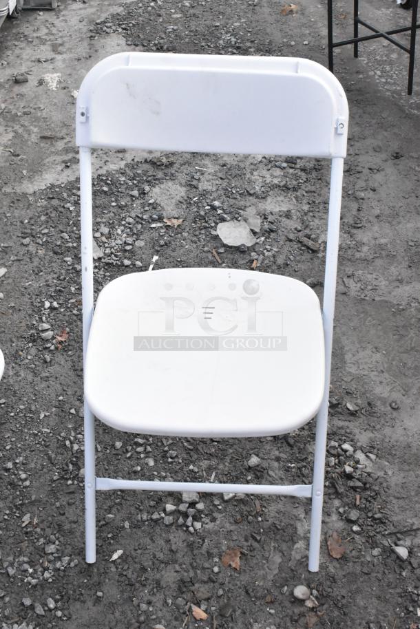 White folding chair with minor scratches on a gravel surface, part of a "scratch and dent" auction lot including a metal basket stand.