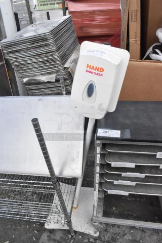 Hand sanitizer dispenser on stand, white with red text, used condition, located in industrial setting.