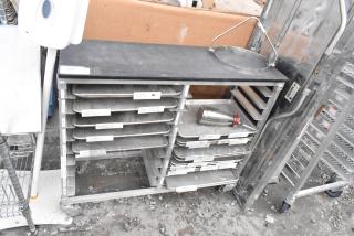 Metal commercial double pan transport rack with multiple metal baking pans, on commercial casters. Some wear visible.